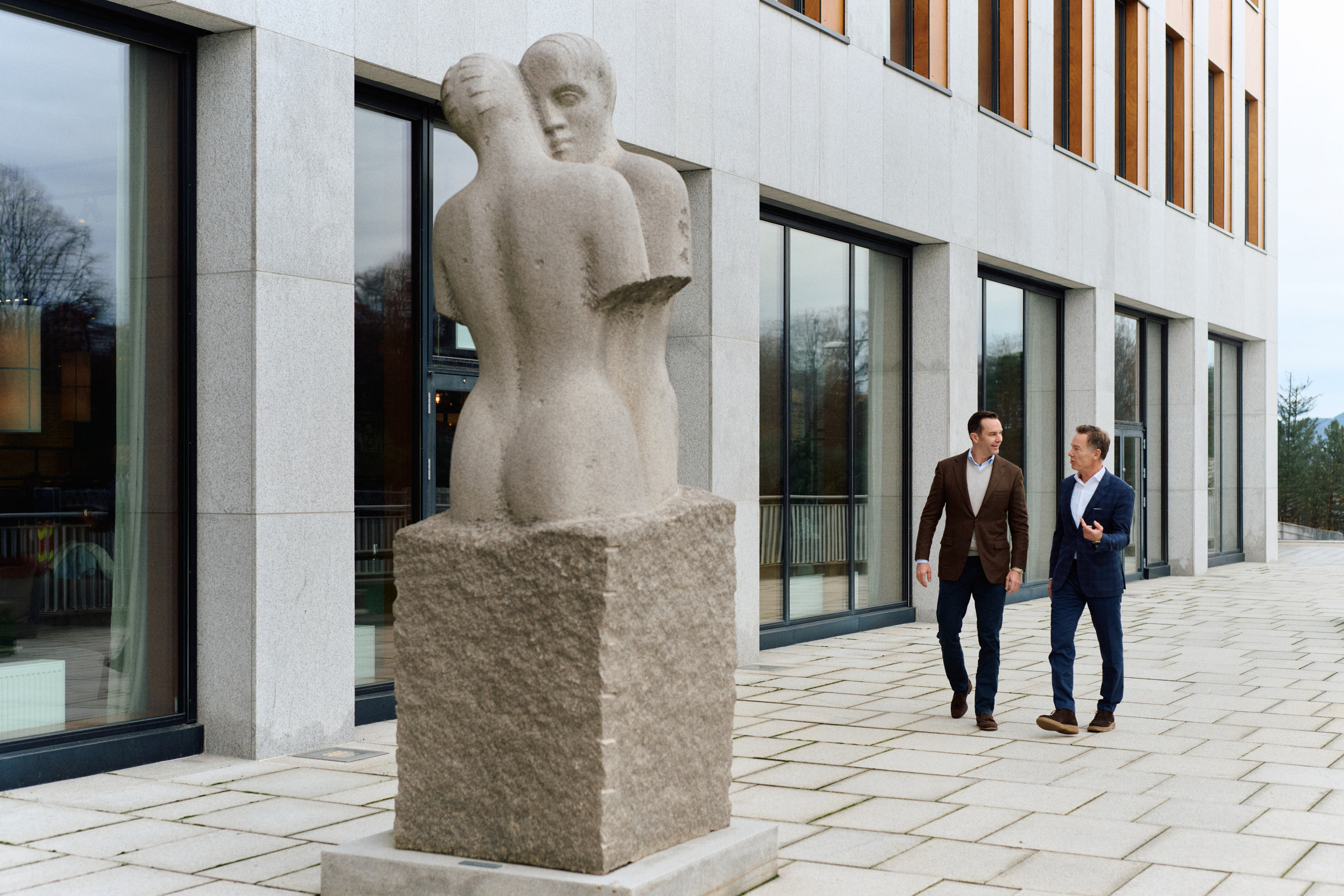 Betongskulptur foran kontorbygg med to personer som går i bakgrunnen.