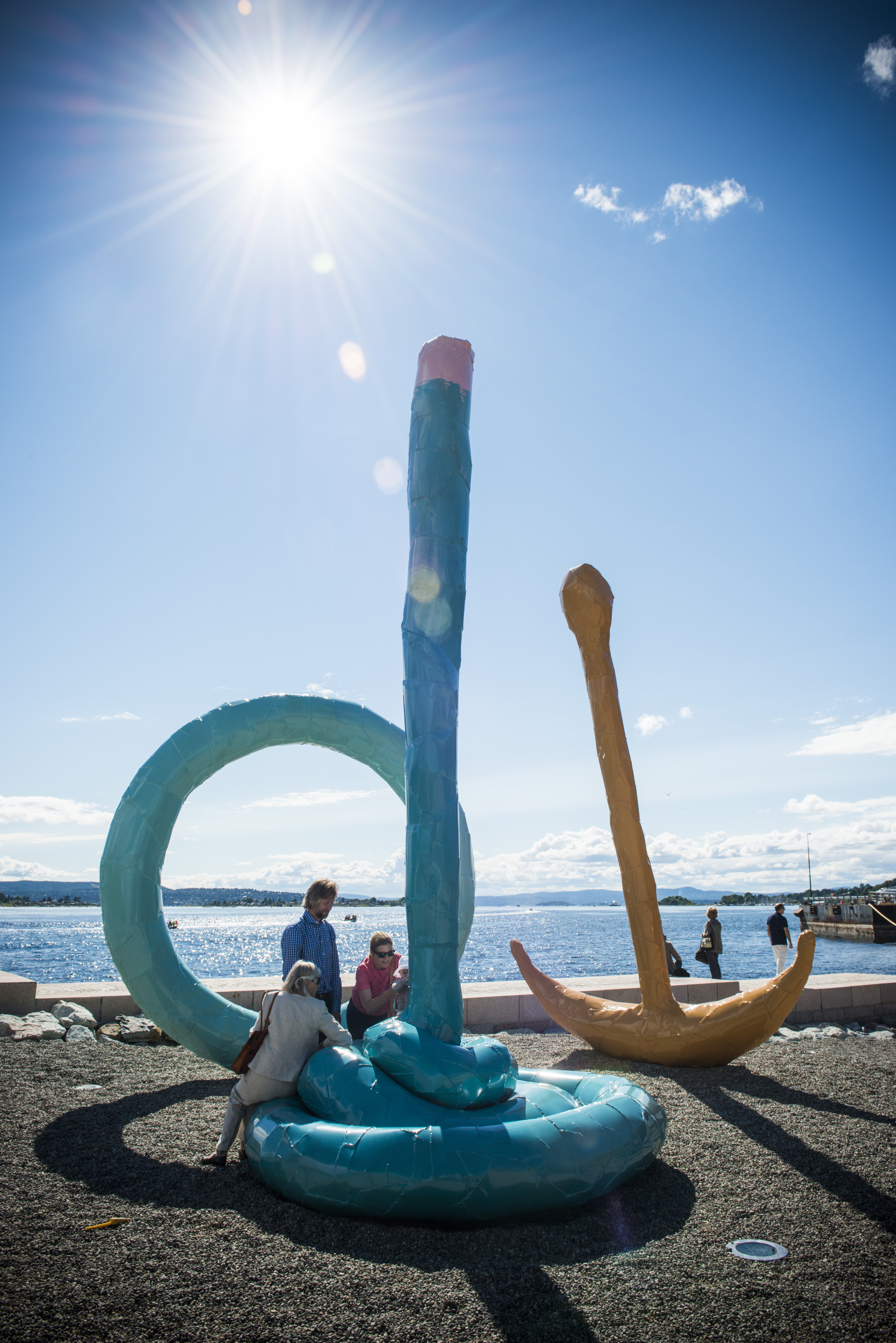 Mennesker som klatrer på skulpturen "Spalt" på Tjuvholmen med fjorden i bakgrunnen.
